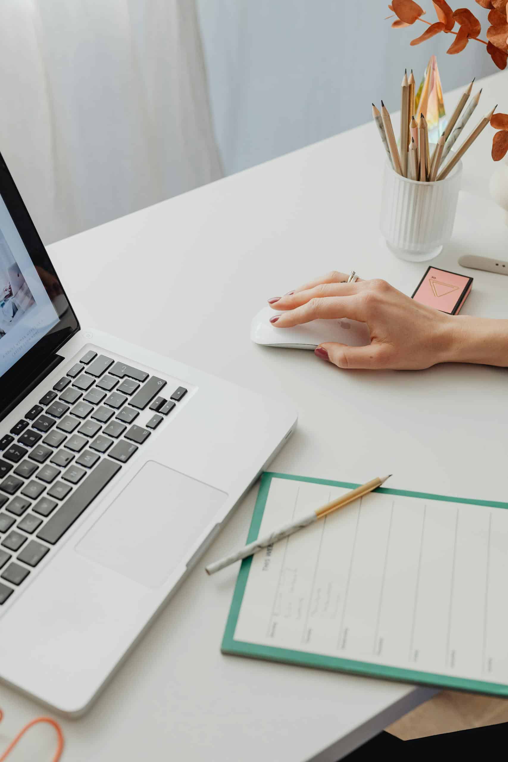 Modern workspace featuring a laptop, planner, and hand on a white desk.